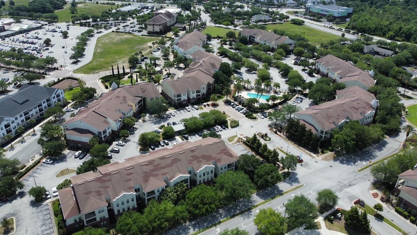 Aerial view of apartment complex with multiple buildings, pool, and parking.