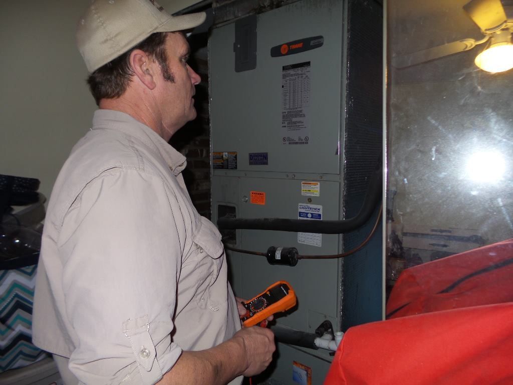 Man in a beige shirt and cap checks a furnace with a multimeter in a room.