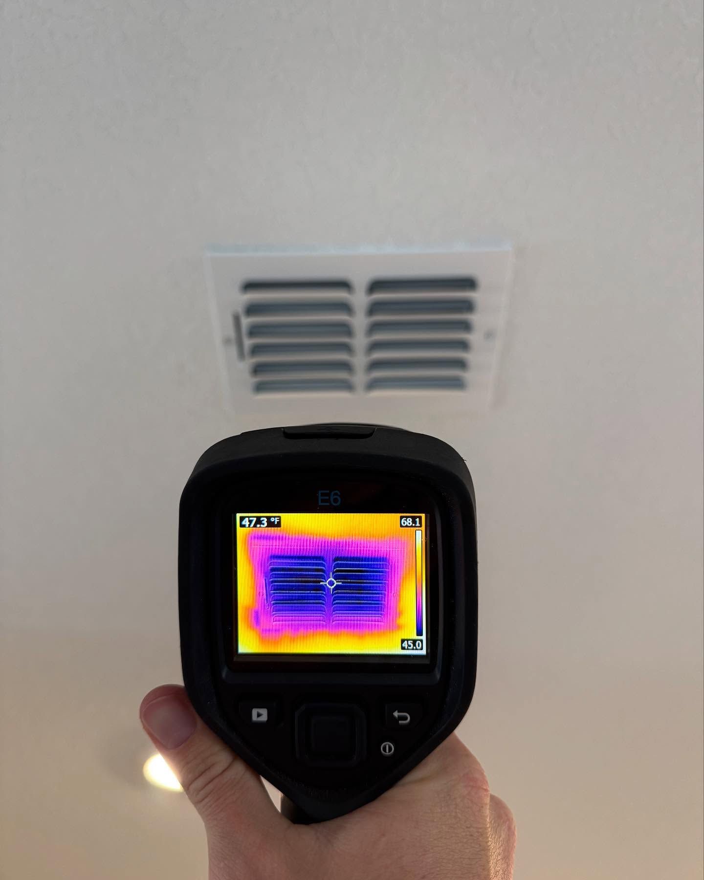 Hand holding thermal camera pointed at ceiling air vent, showing temperature variations.