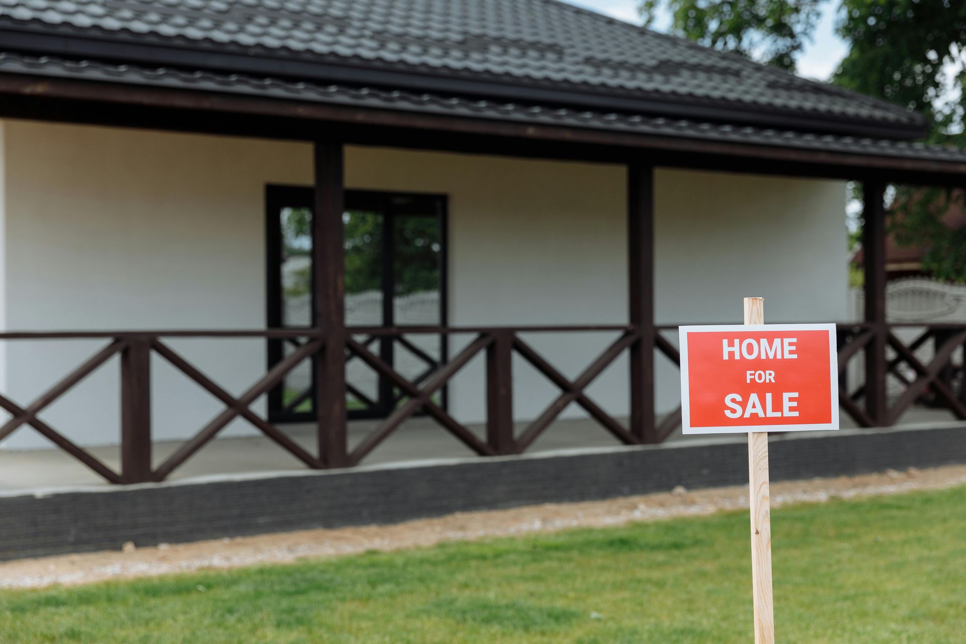 Home for sale sign in front of a white house with a brown porch and a green lawn.