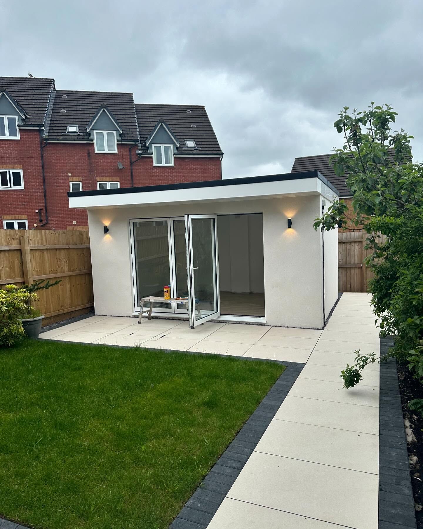A white building with sliding glass doors is in the backyard of a house.