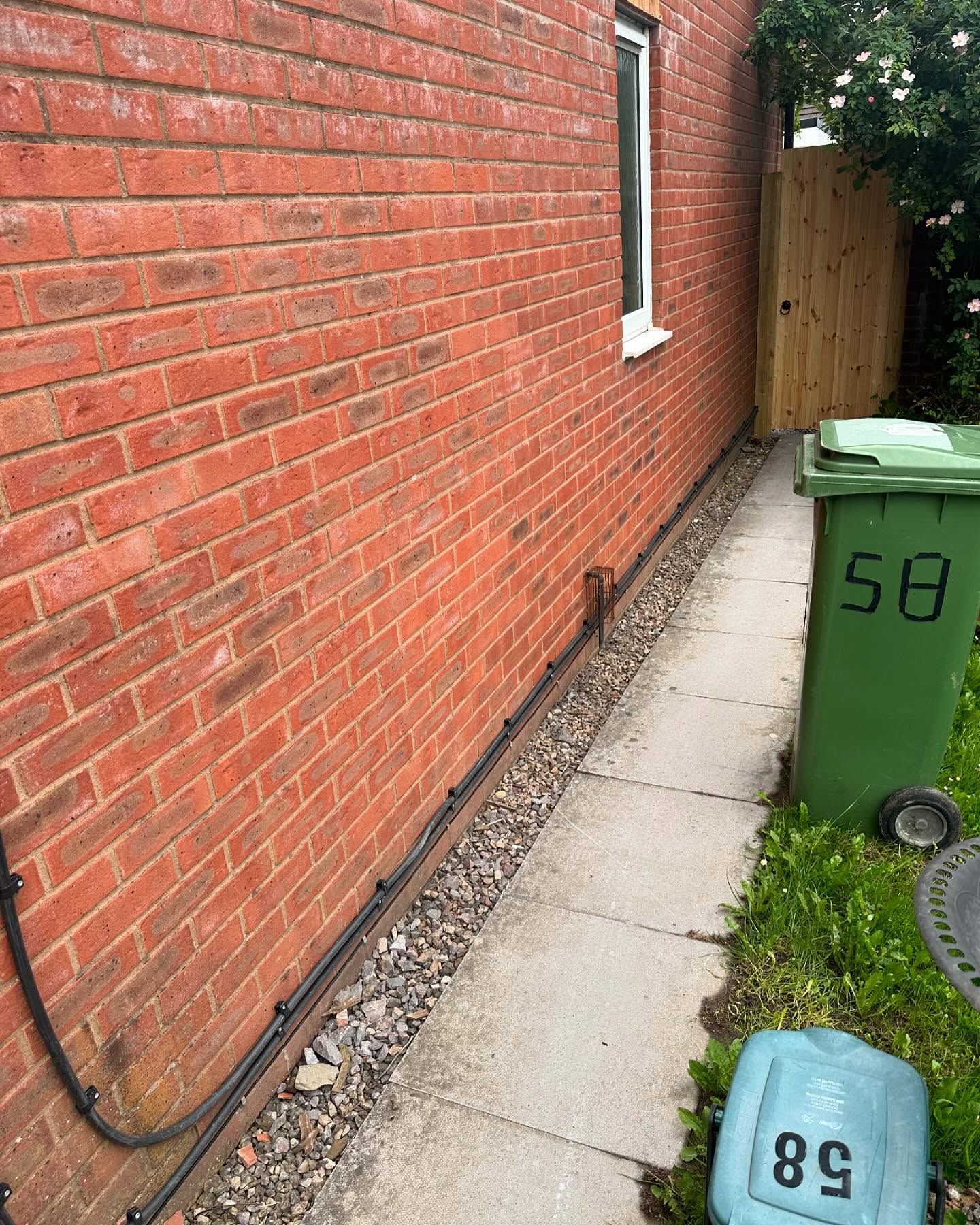 A brick wall with a green trash can in front of it.