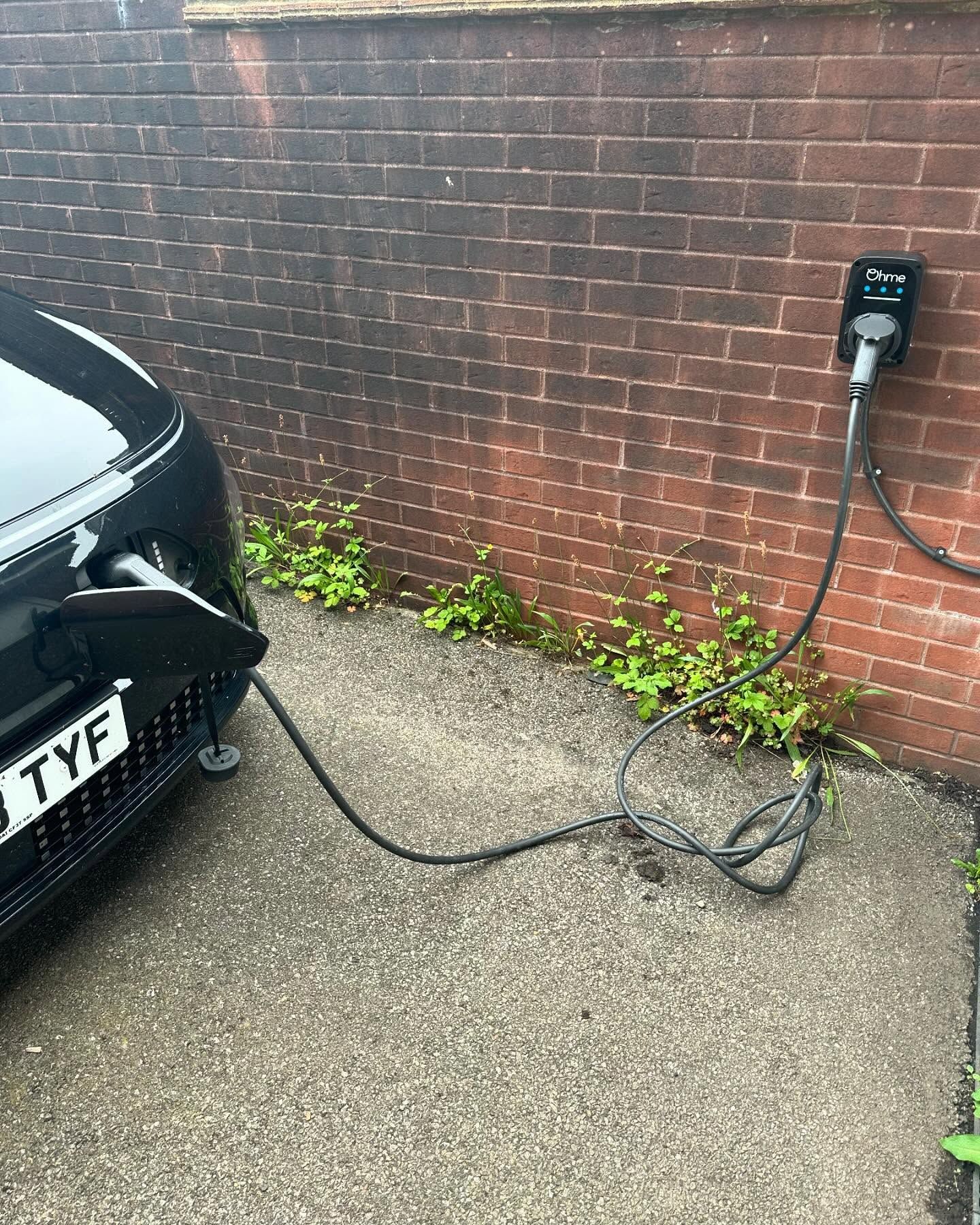 A car is being charged at a charging station in front of a brick wall.