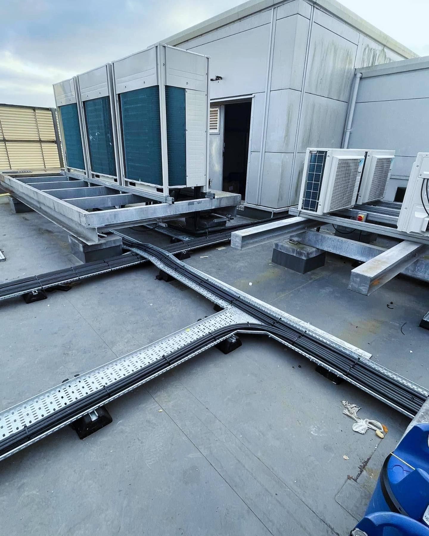 A blue car is parked in front of a building with a lot of air conditioners on the roof.
