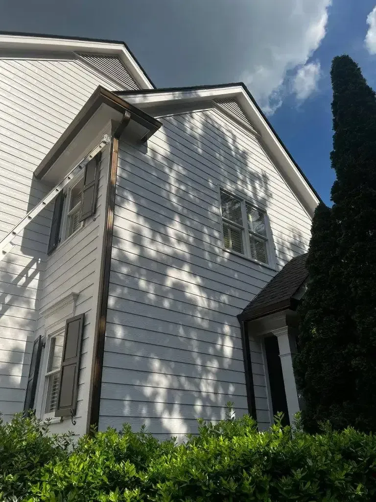 White house with brown trim and shutters, against a cloudy blue sky.