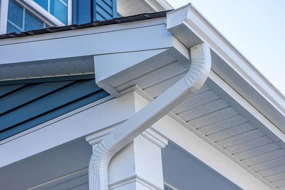 White gutters and downspout on a house with blue siding.