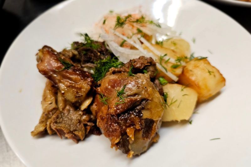 A white plate topped with meat and potatoes on a table