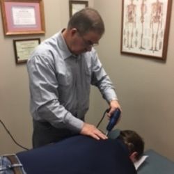 A man is using a tool on a man 's back in a room.