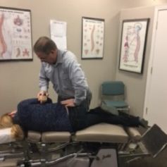 A man is adjusting a woman 's back on a table in a room.