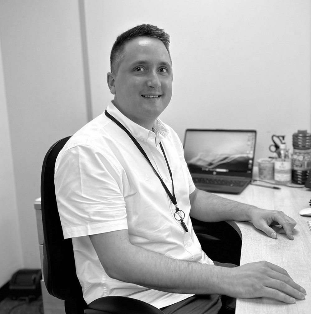 A man in a white shirt is sitting at a desk with a laptop