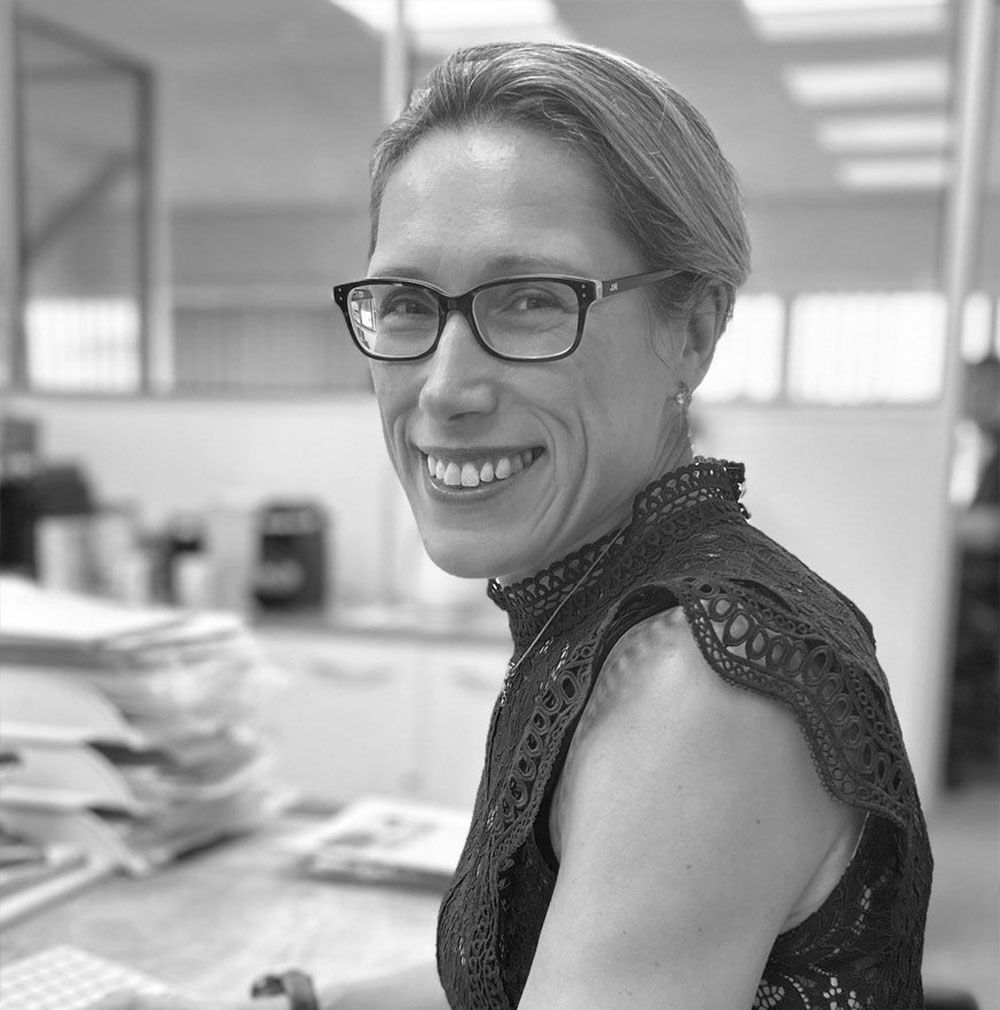 A woman wearing glasses is smiling in a black and white photo.