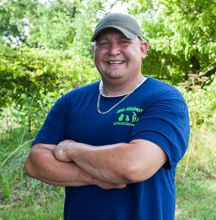 A man wearing a blue shirt and a hat is smiling with his arms crossed