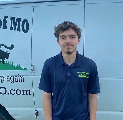 A young man in a blue shirt is standing in front of a white van.