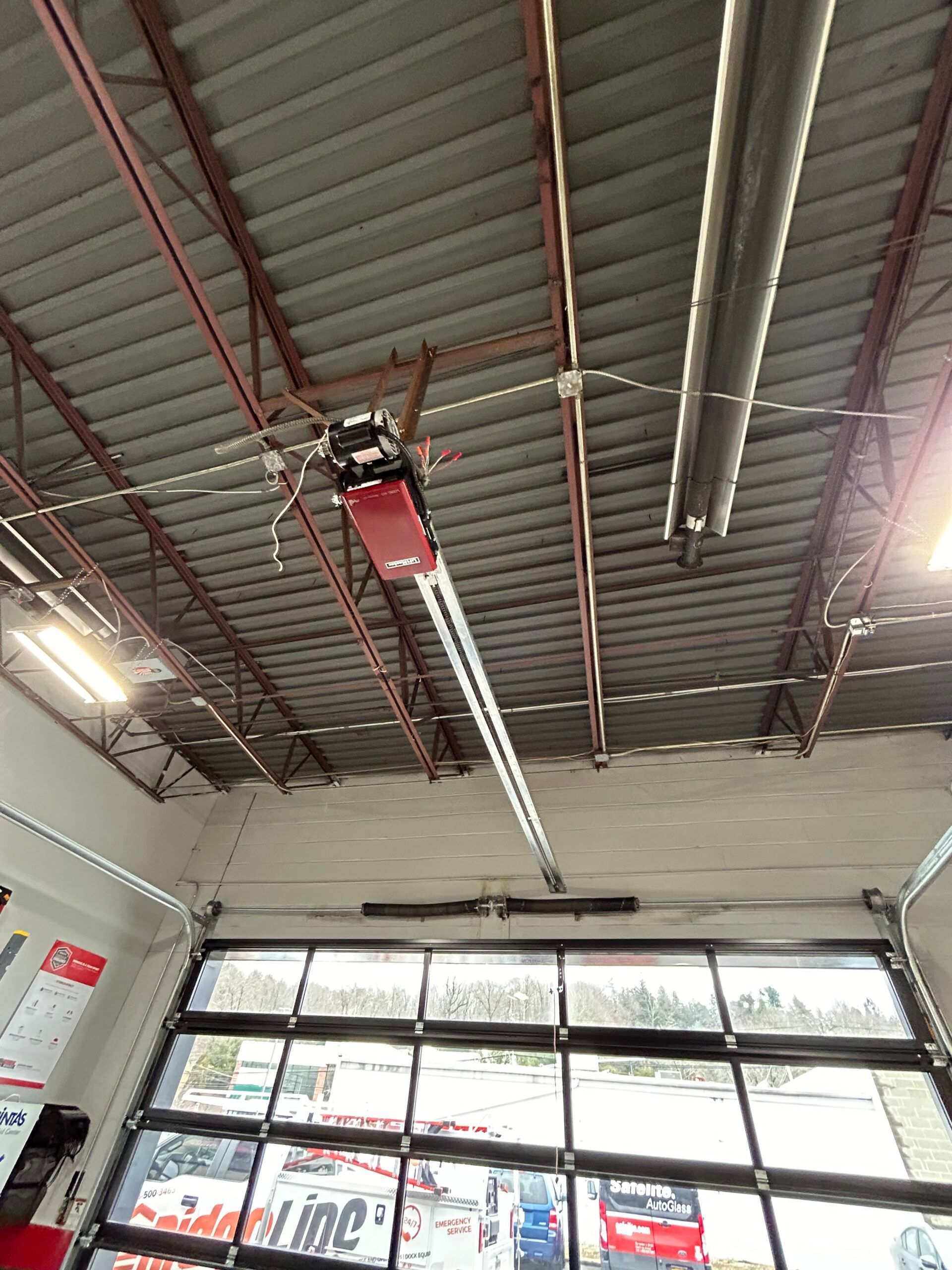 Red overhead garage door opener on a warehouse ceiling above glass storefront doors