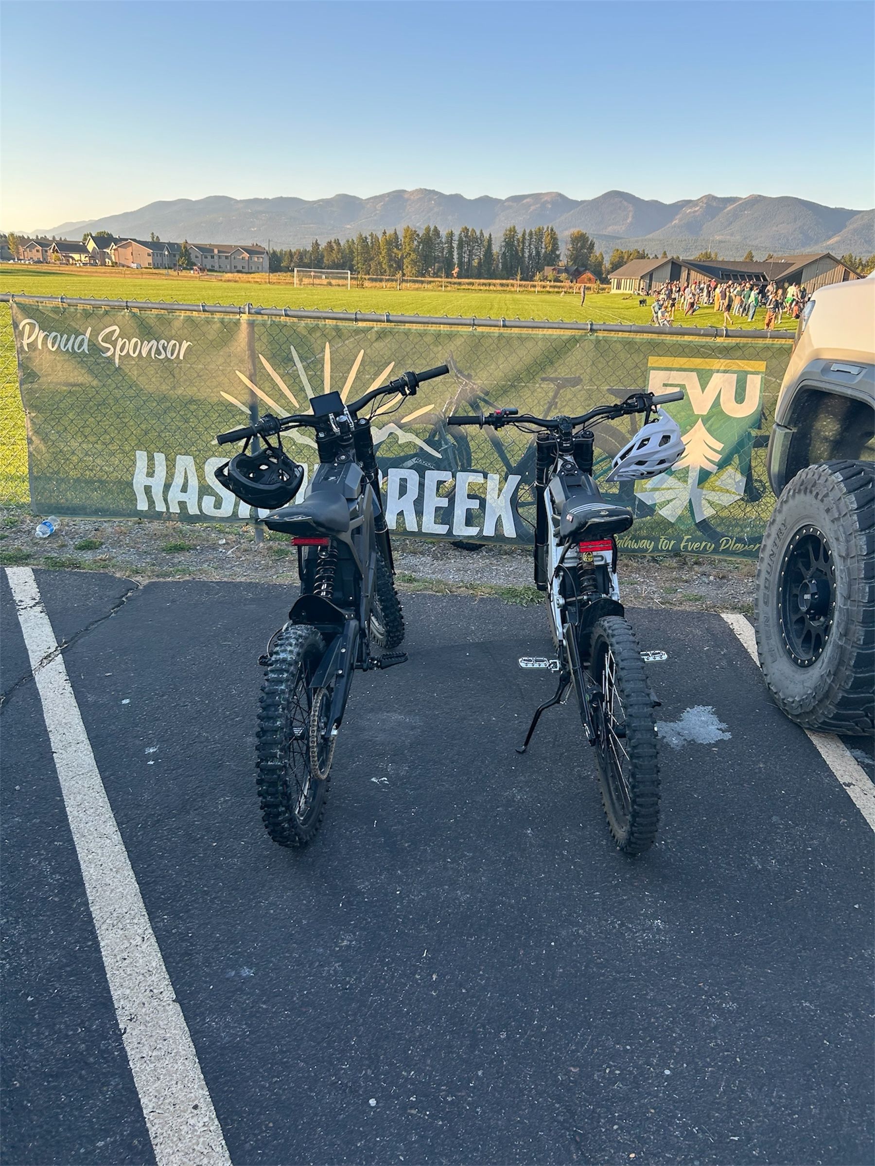 Two black electric motorcycles parked in a parking lot, with mountains in the background.