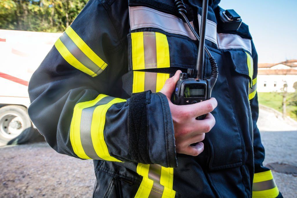 Firefighter in dark coat with yellow stripes, holding a two-way radio.