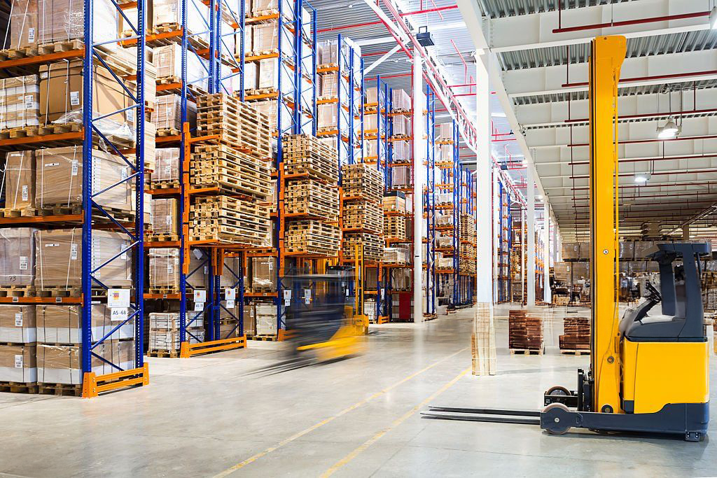 Warehouse interior with tall shelving, boxes, and a yellow forklift.