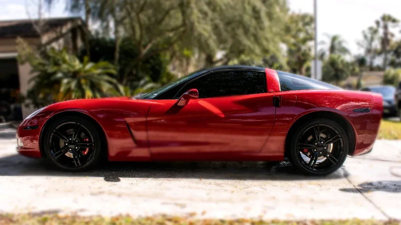 Red Chevrolet Corvette coupe with black roof and wheels parked outside on a sunny day.