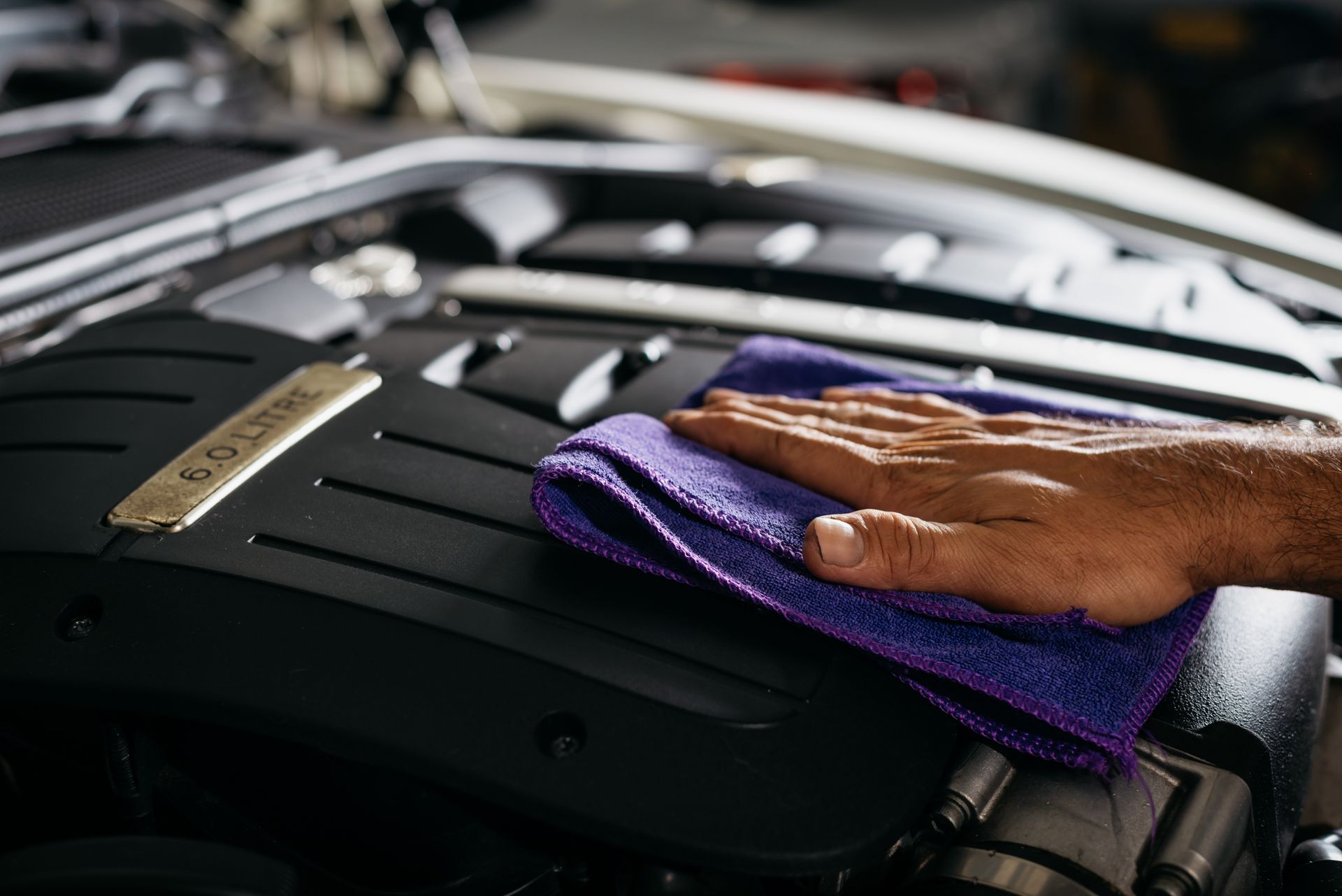 Hand wiping a black car engine with a purple microfiber cloth.