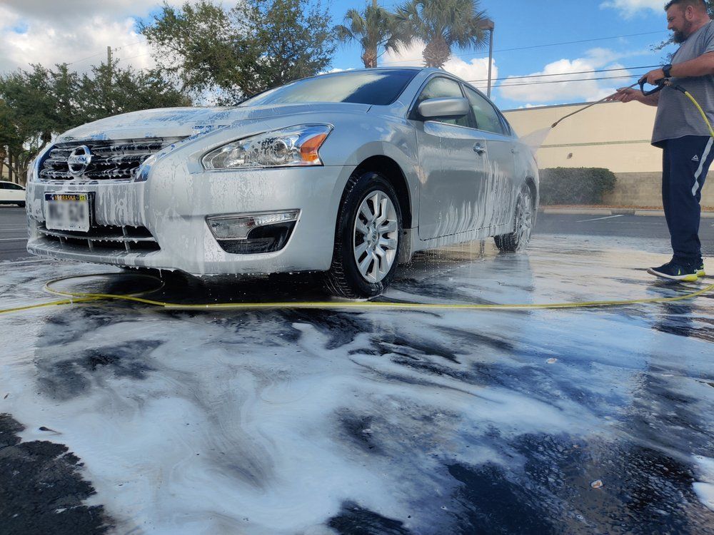 A person washing a silver car with soapy water at a car wash.