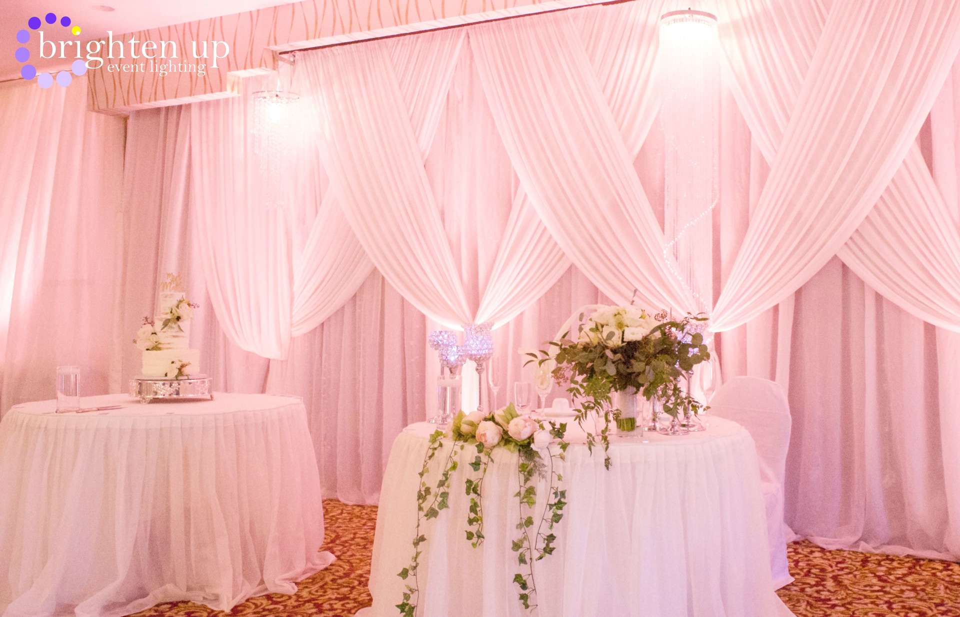 A table with flowers on it is in front of a pink curtain.