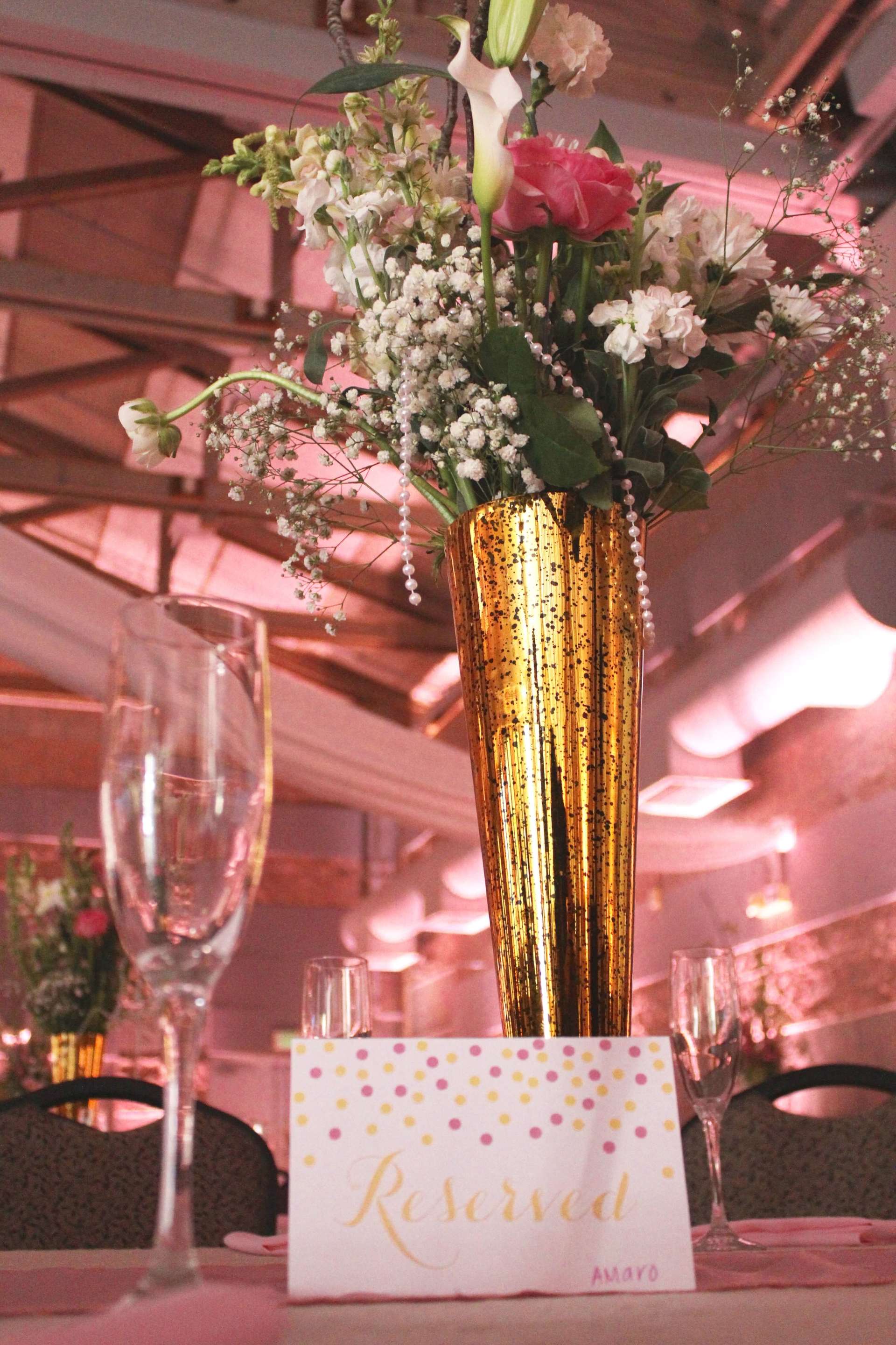 A gold vase filled with flowers sits on a table next to a reserved sign