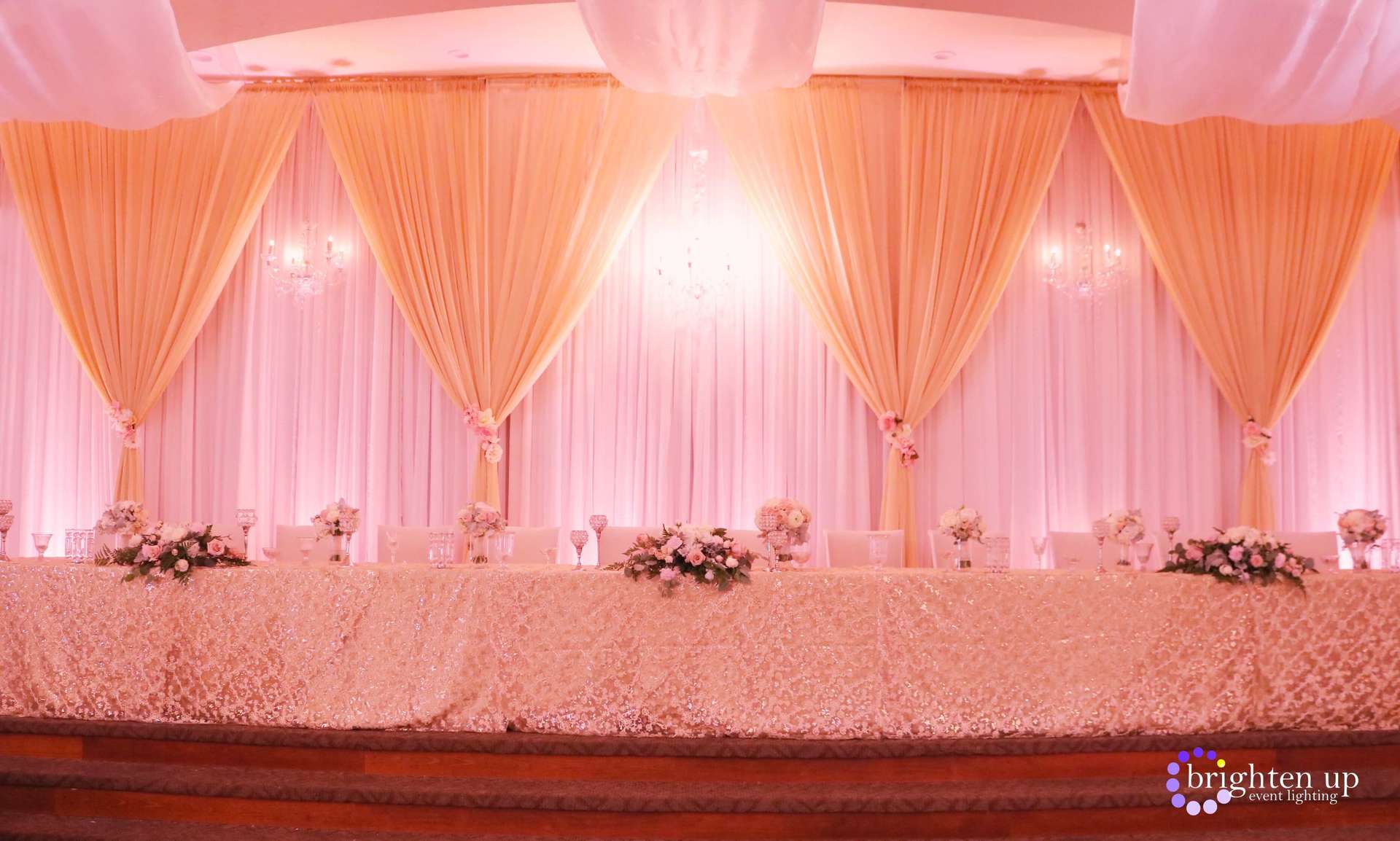 A long table with a pink and white backdrop and flowers on it.