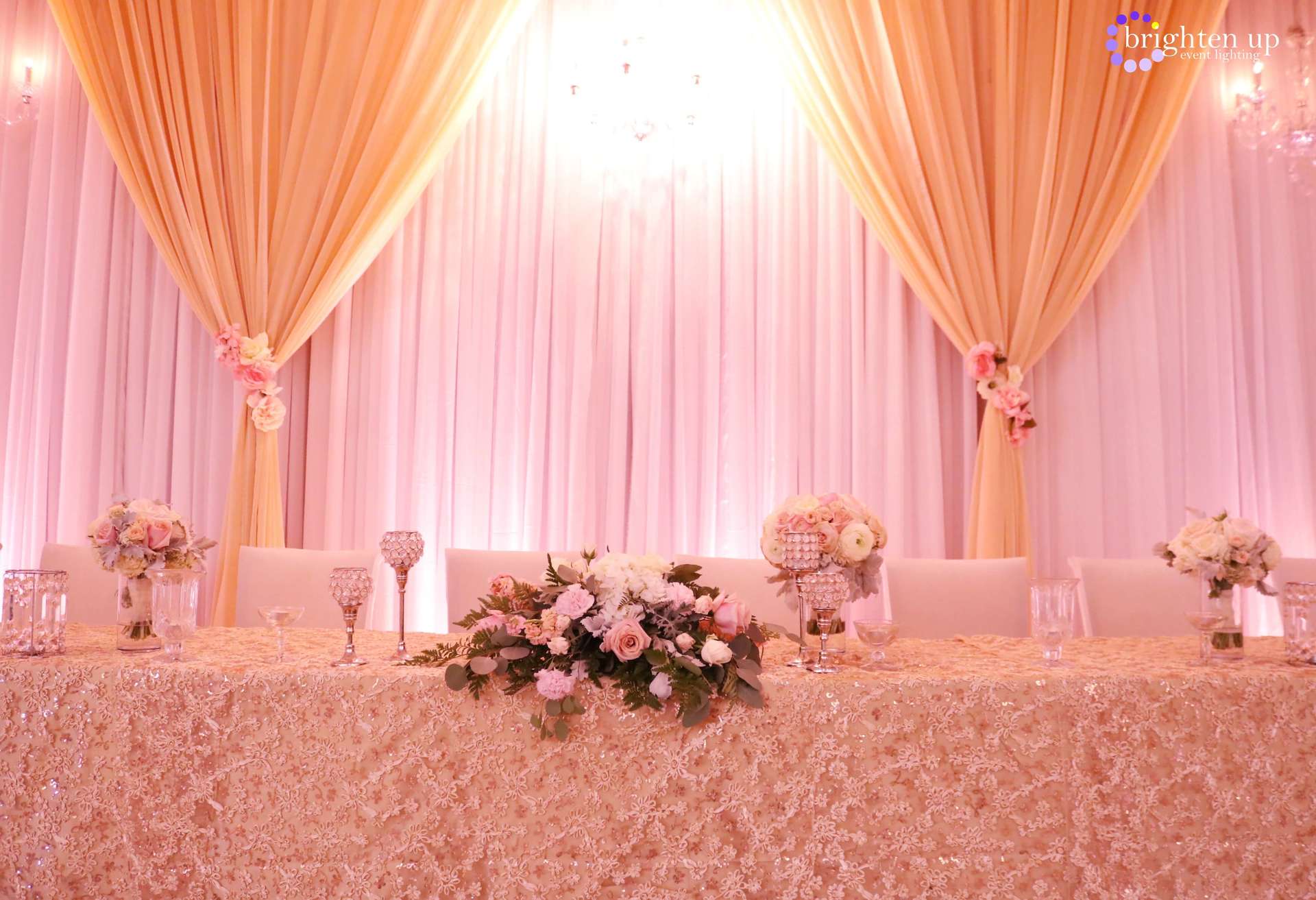 A long table with flowers on it in front of a pink curtain.