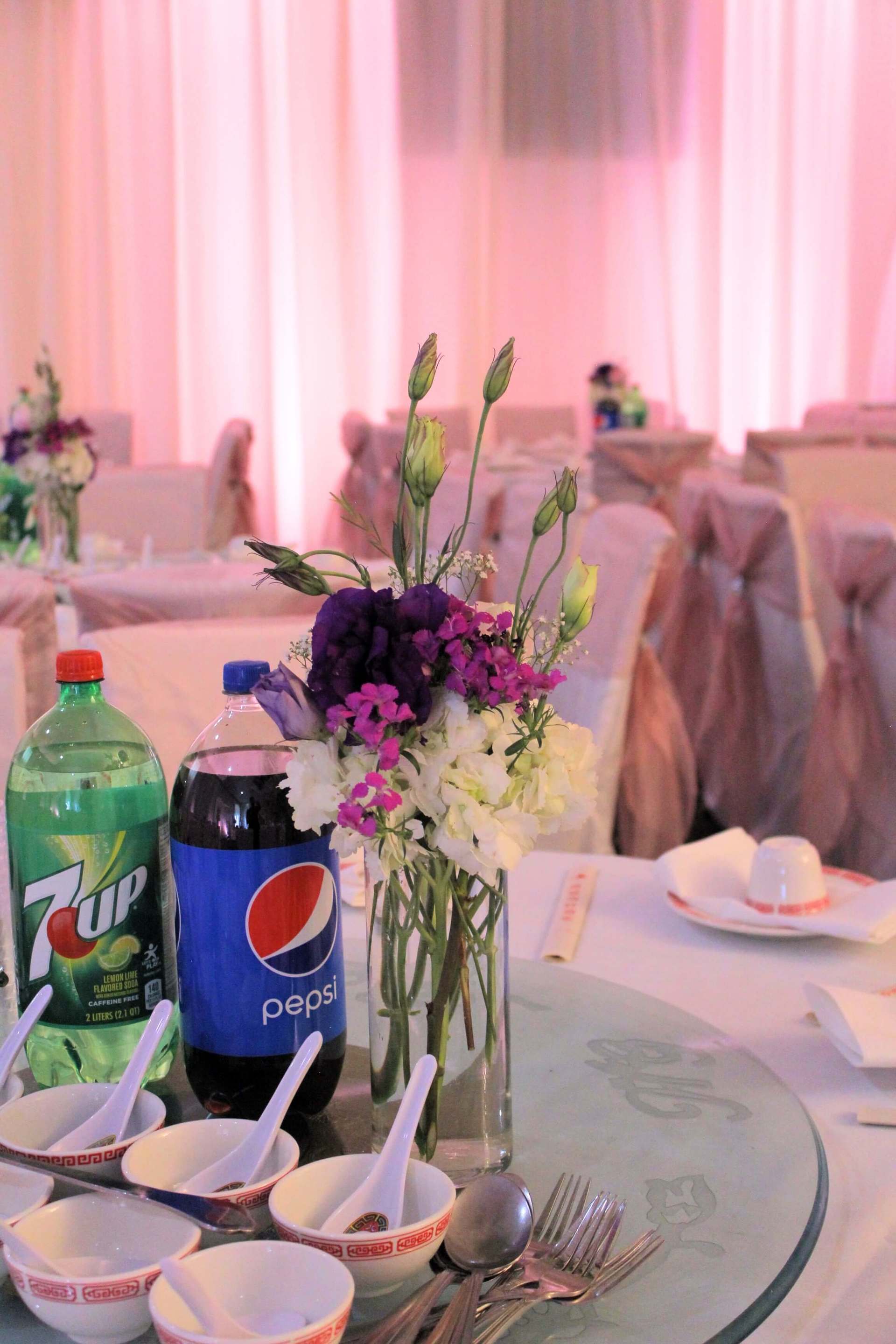 A table with a vase of flowers and a bottle of pepsi on it.
