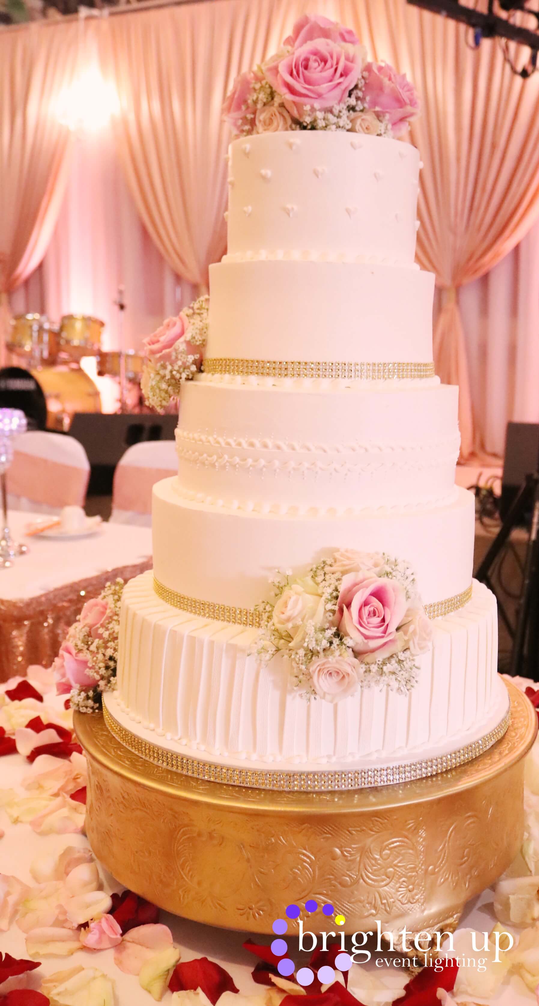 A wedding cake is sitting on top of a gold cake stand on a table.