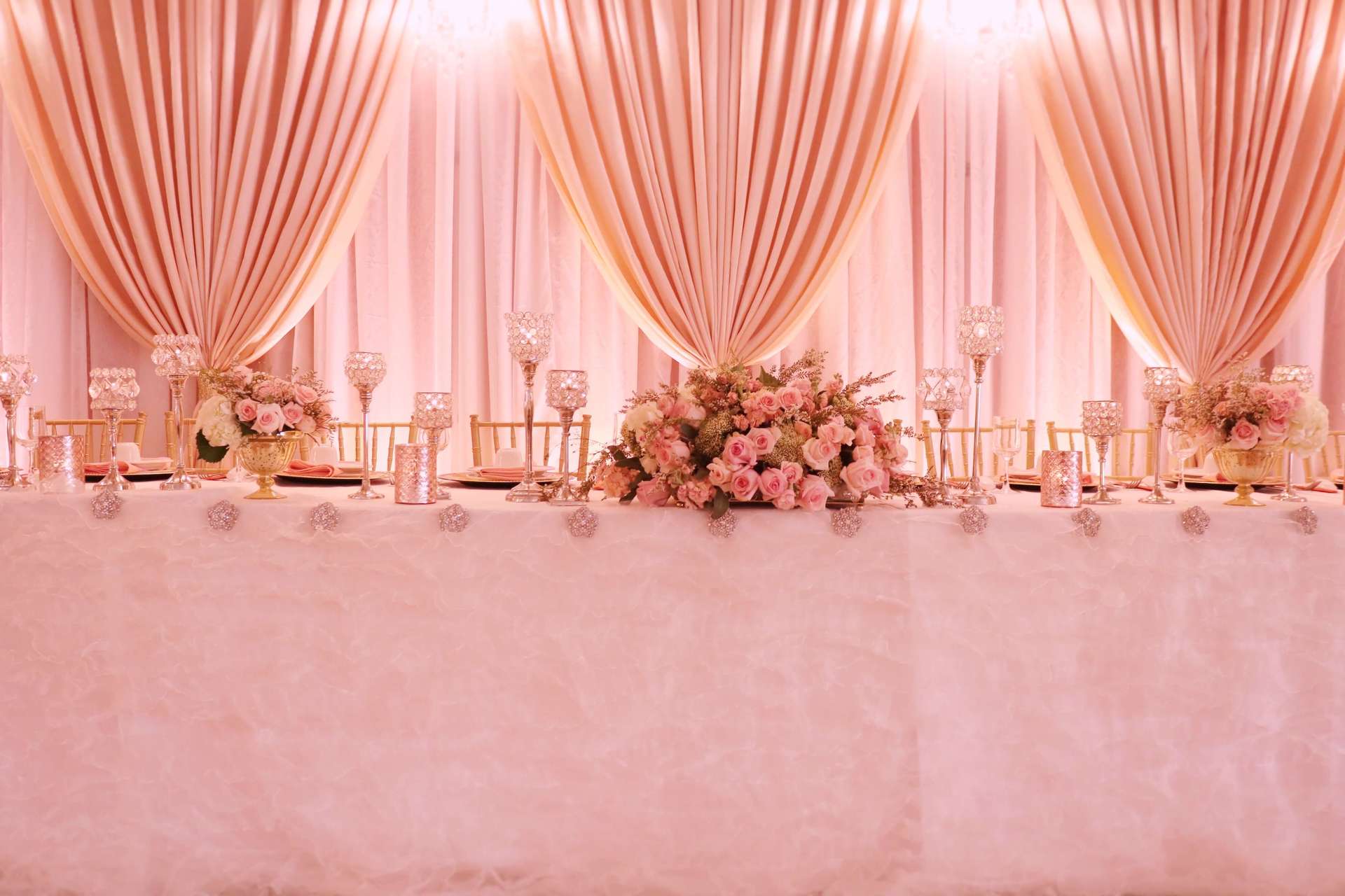 A long table with flowers and candles on it in front of a pink curtain.
