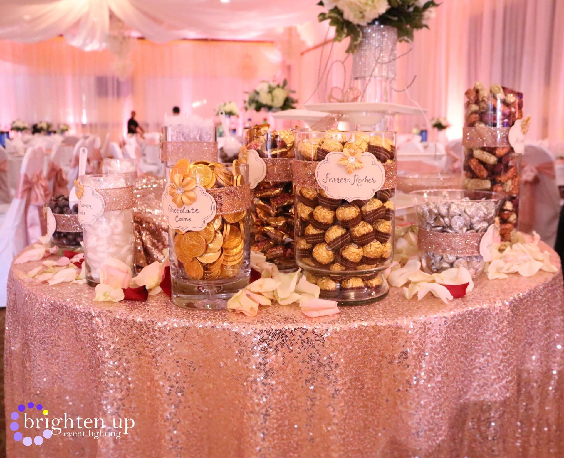 A table with a sequined tablecloth and jars of candy on it.