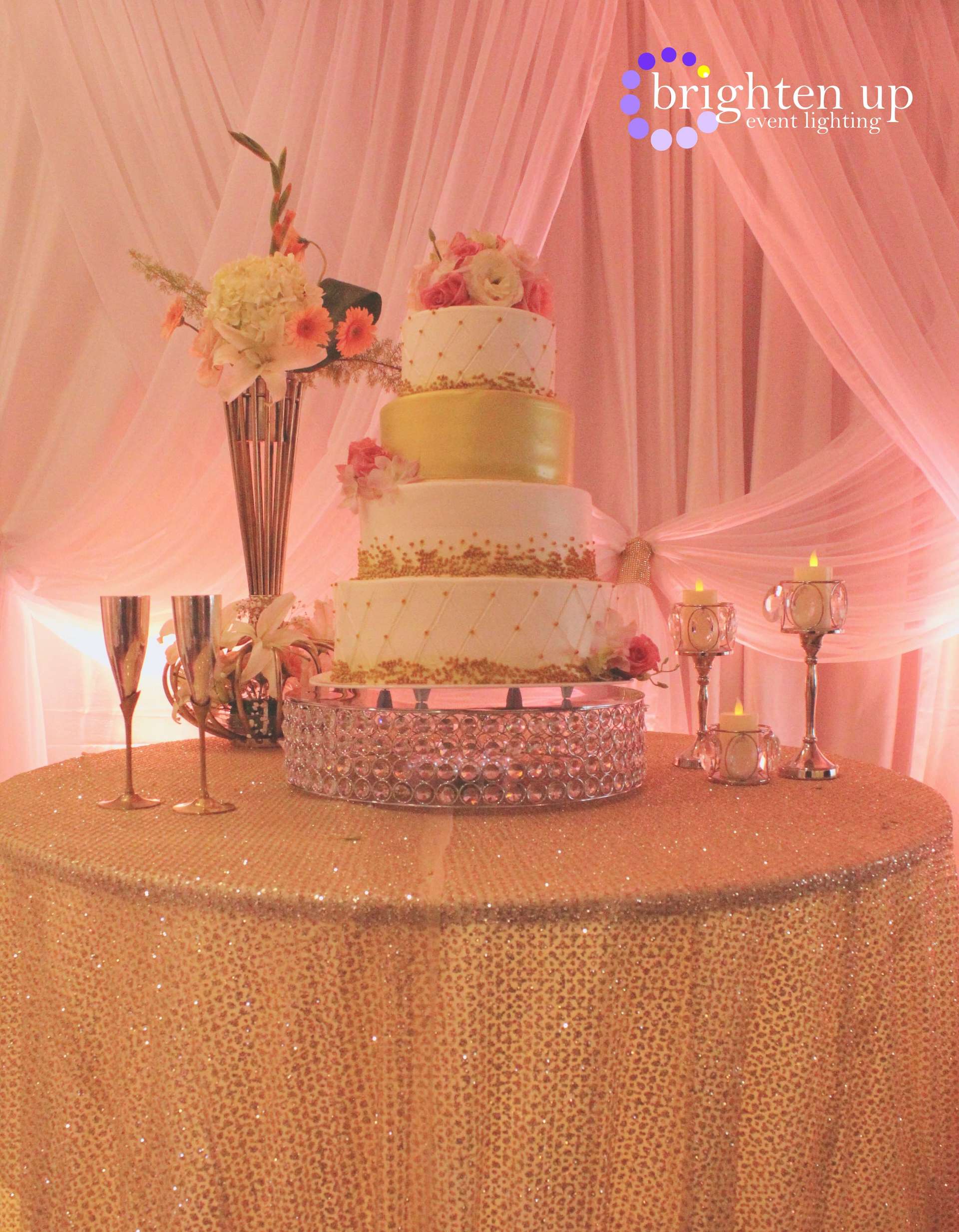 A wedding cake is sitting on top of a table with a gold tablecloth.