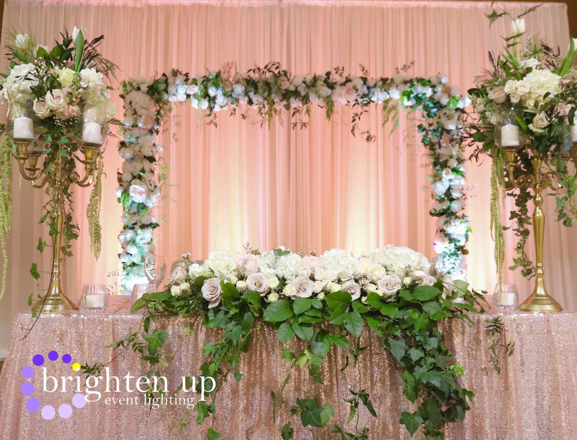 A table with flowers and candles on it in front of a pink curtain.
