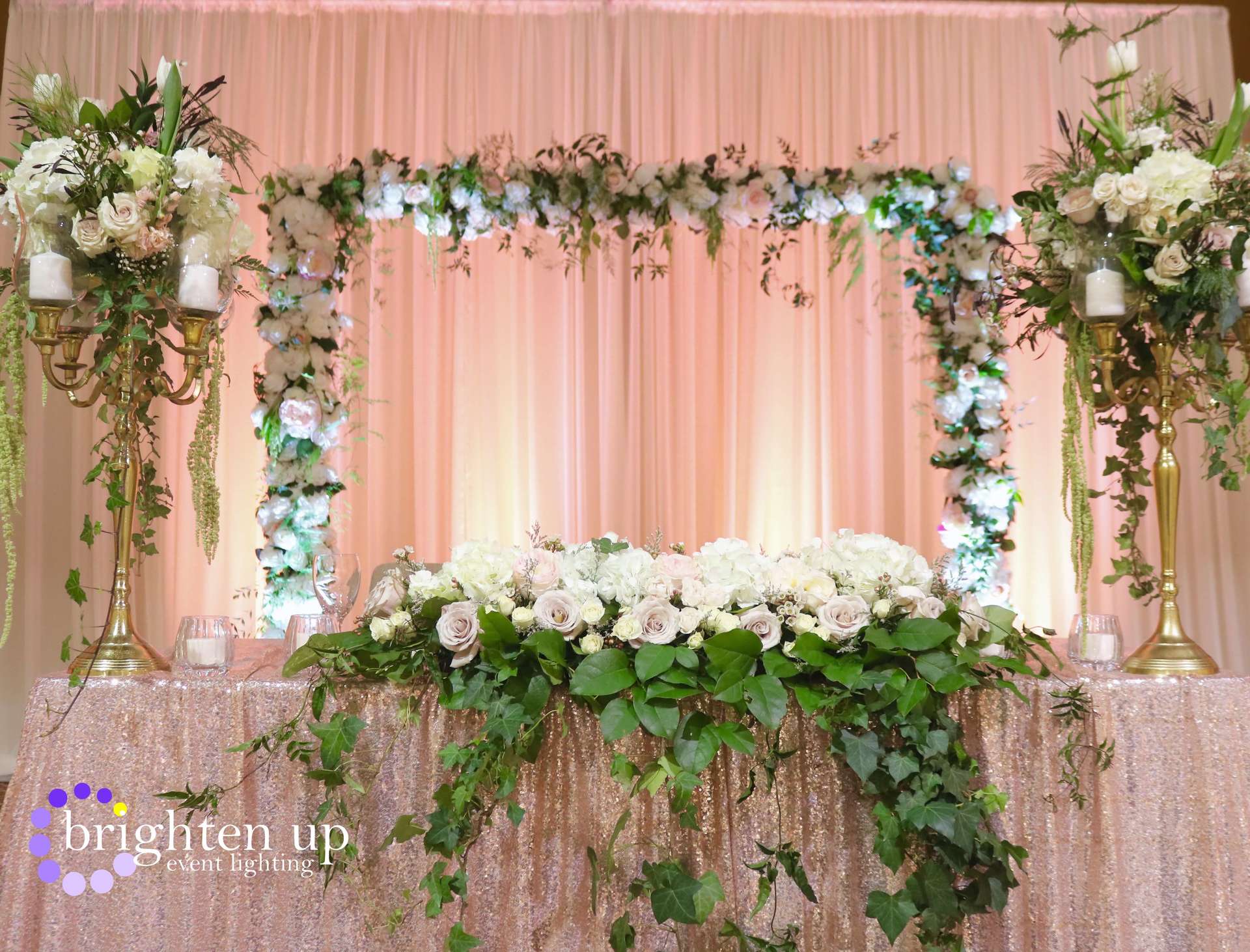 A table with flowers and candles on it in front of a pink curtain.