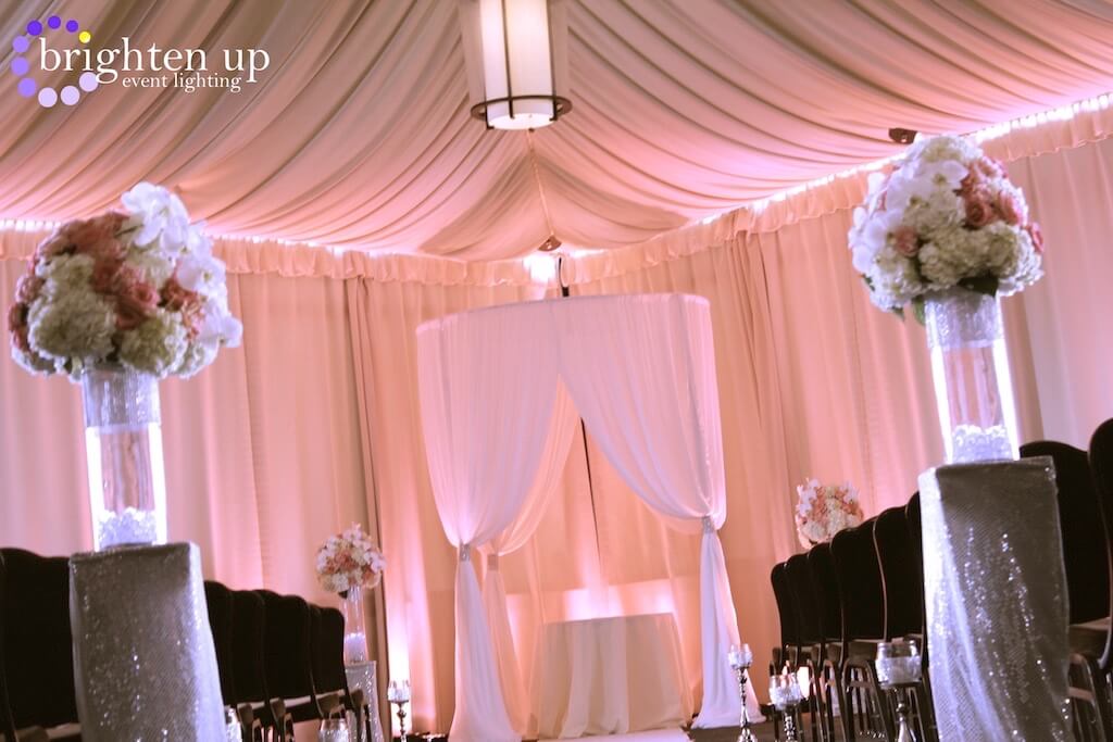 A wedding ceremony is being held under a pink canopy