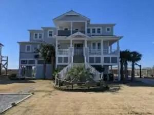 A large white house is sitting on top of a sandy beach.