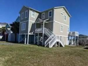 A large house with stairs leading up to it is sitting on top of a lush green field.