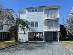 A large white house with a lot of windows and balconies is sitting on top of a gravel driveway.