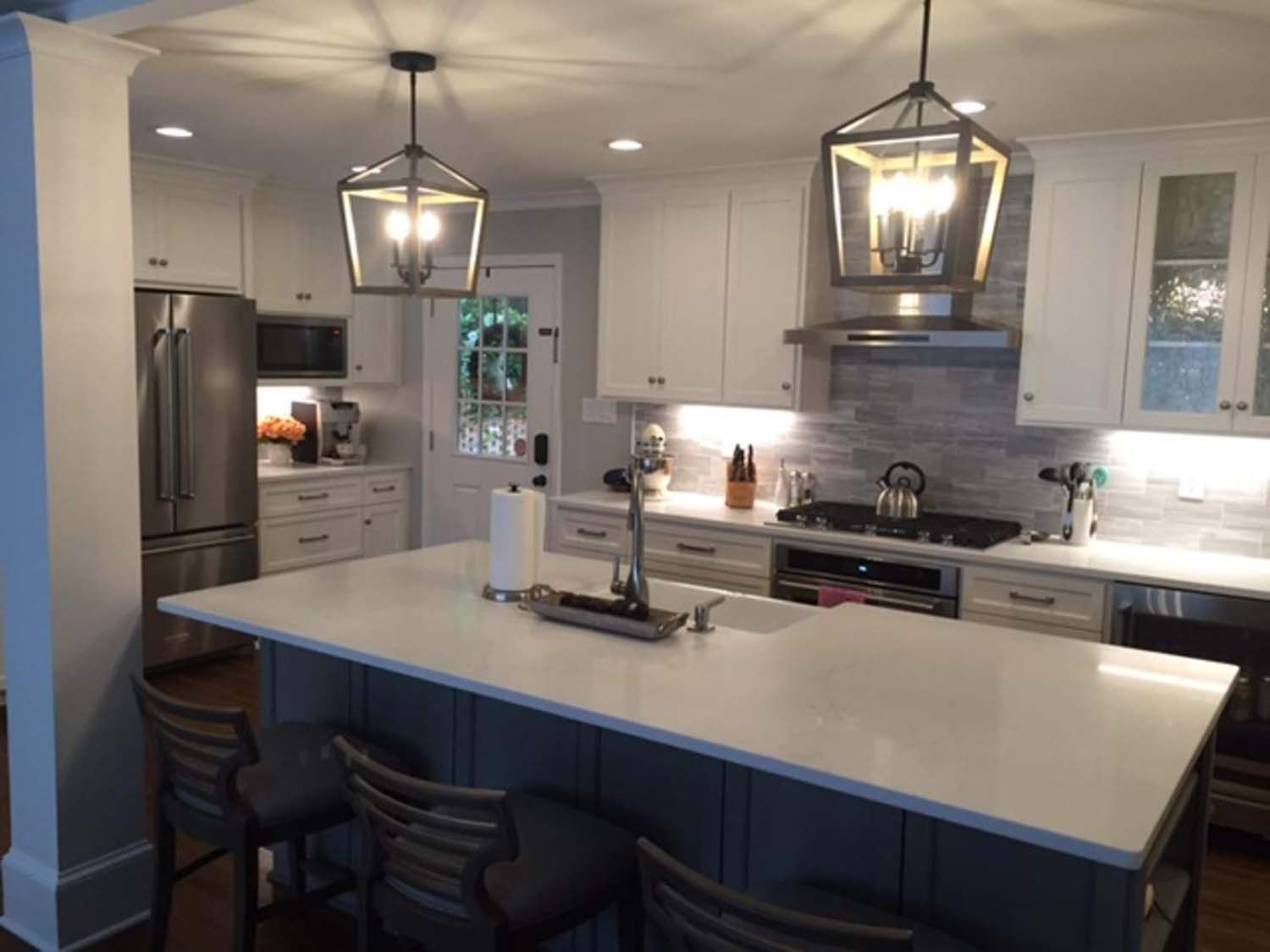 Modern kitchen with white cabinets, gray island, pendant lights, and stainless steel appliances.