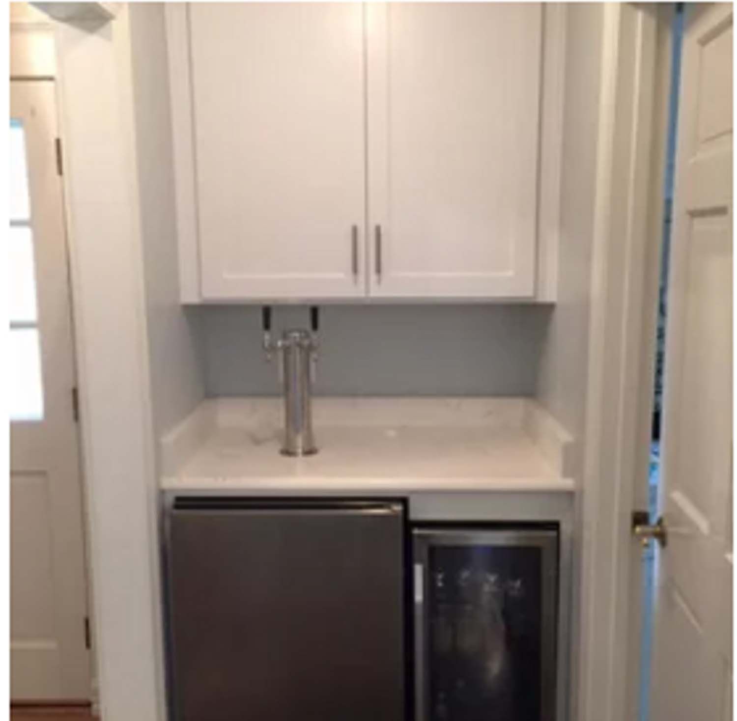 A white built-in home bar area with a tap, mini-fridges, and cabinets.