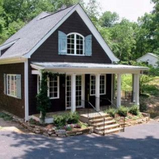 Brown cottage with white porch, blue shutters, and small garden.