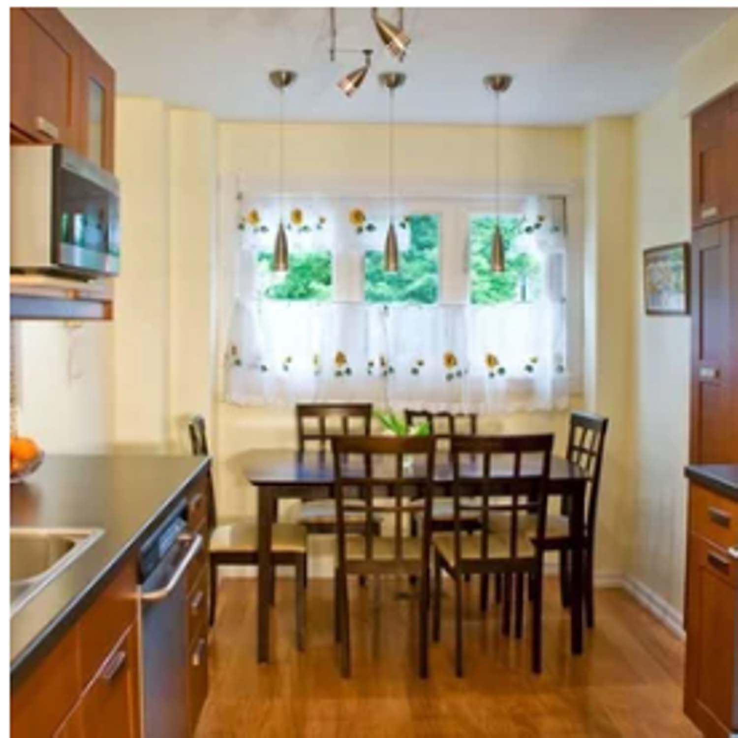Kitchen with a dark wood table and chairs, wooden cabinets, and a window with sheer curtains.