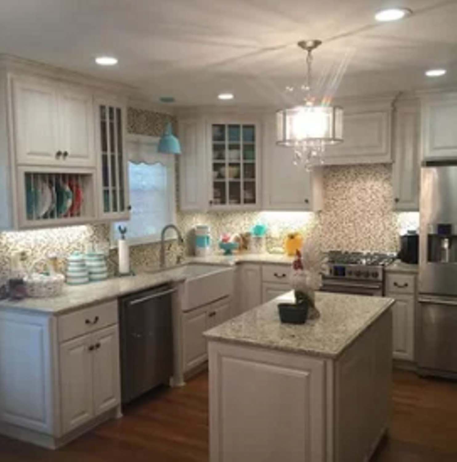 Bright, white kitchen with island, stainless steel appliances, and decorative backsplash; hardwood floors.