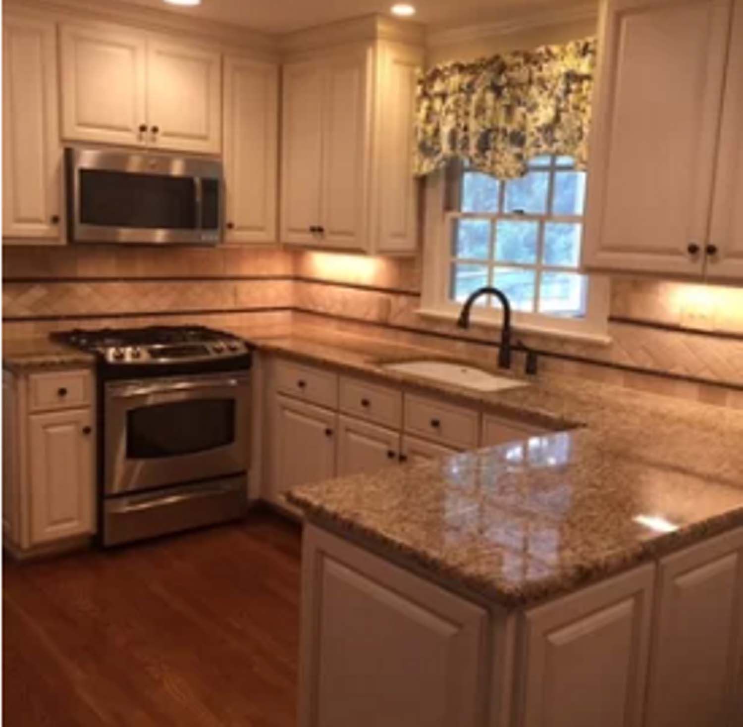 Cream-colored kitchen with granite countertops, stainless steel appliances, and a window with floral valance.