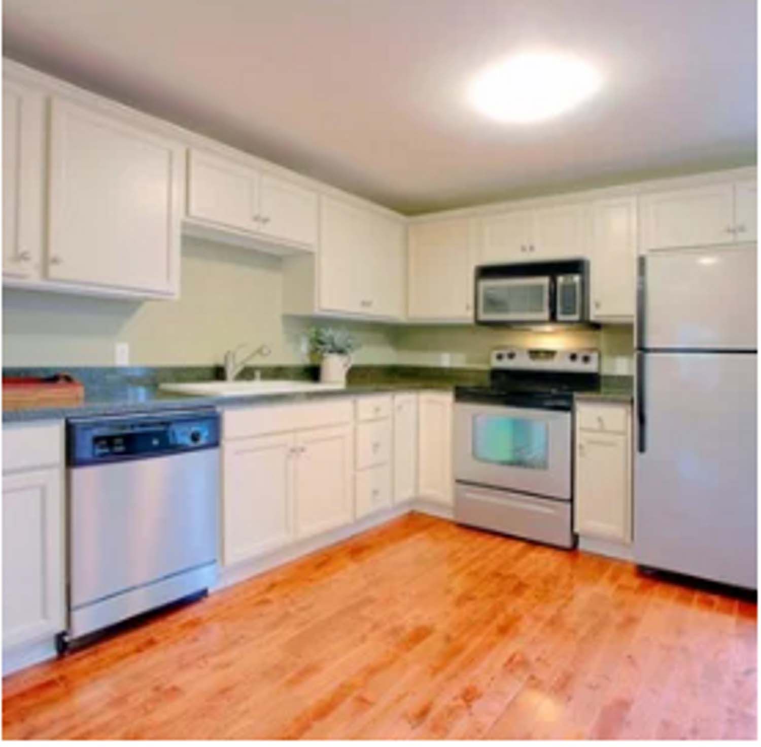 Kitchen with white cabinets, stainless steel appliances, wood floor.