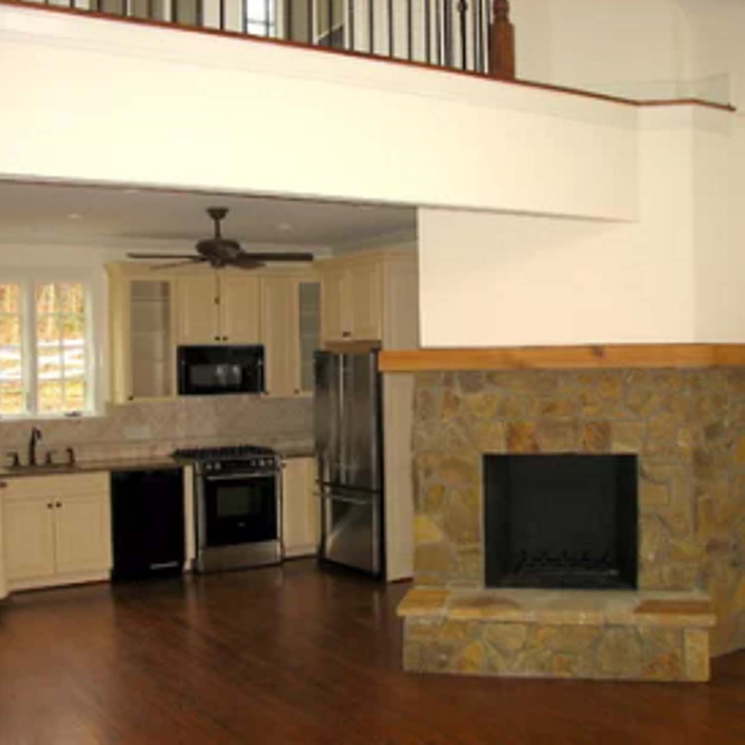 Open concept kitchen and living area with a stone fireplace and hardwood floors.