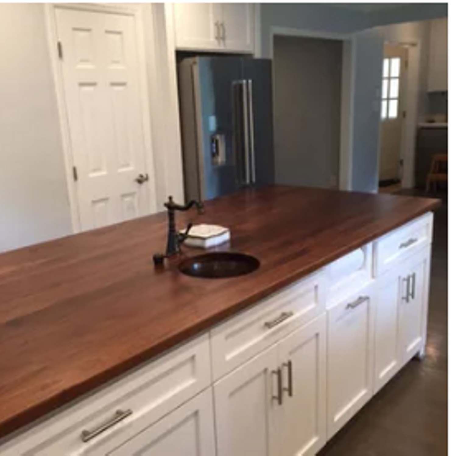 White kitchen island with a wooden countertop, bronze sink, and stainless steel refrigerator.