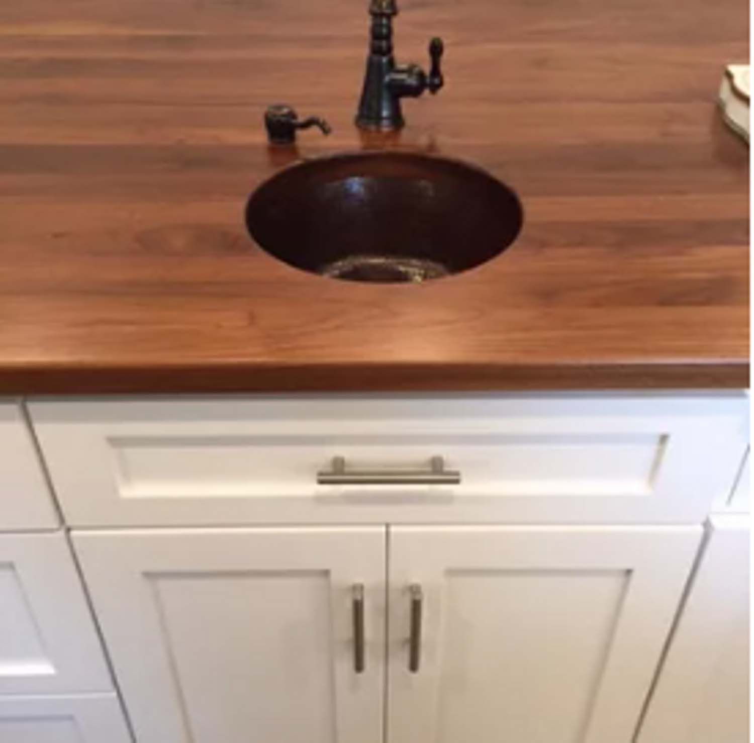 White cabinets with a brown wooden countertop featuring a copper sink and black faucet.