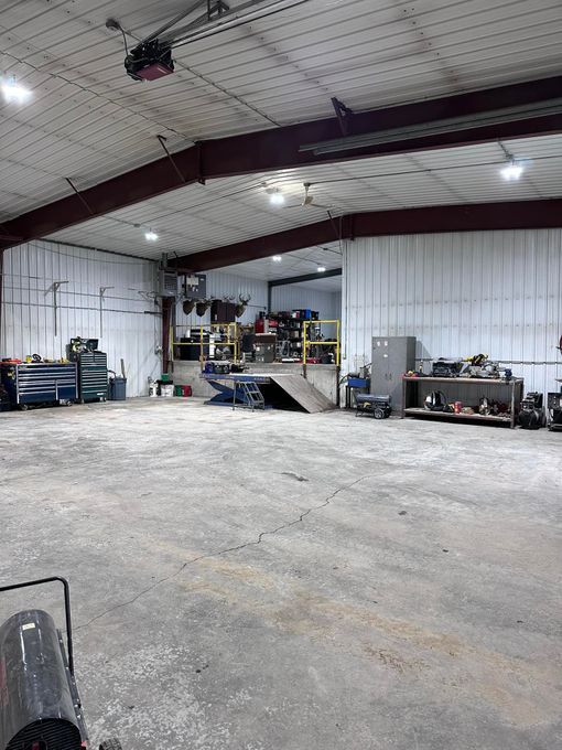 Large, empty auto repair shop with a concrete floor, equipment, and tools. Overhead garage door closed.